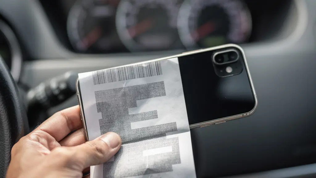 Main tenant un smartphone photographiant un ticket de caisse sur tableau de bord avec jauge visible